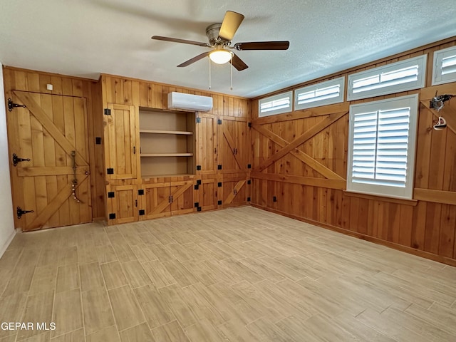 interior space featuring an AC wall unit, wooden walls, ceiling fan, and a textured ceiling