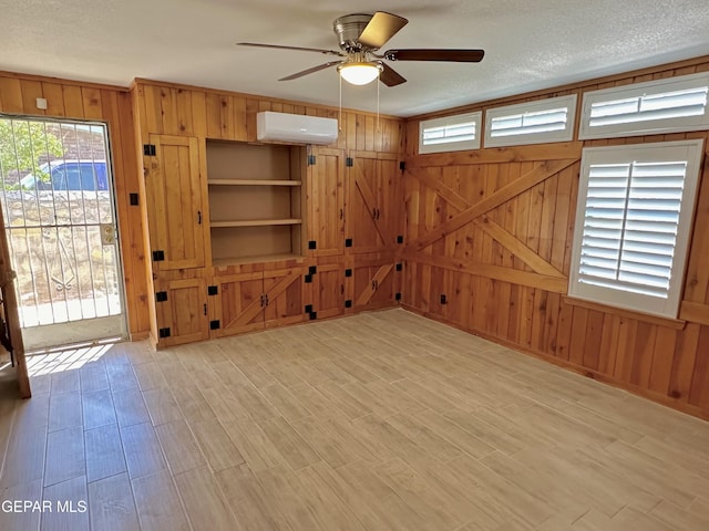 unfurnished living room with a wealth of natural light, a textured ceiling, a wall mounted AC, and ceiling fan