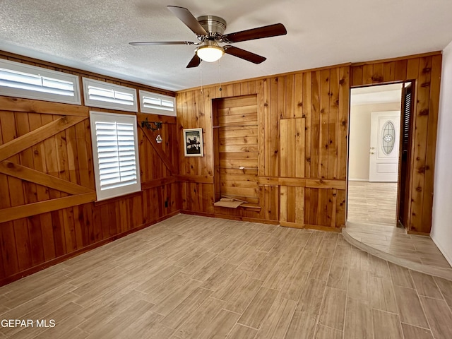 spare room featuring a textured ceiling, light hardwood / wood-style floors, ceiling fan, and wood walls