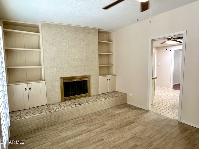 unfurnished living room with built in features, light hardwood / wood-style flooring, a textured ceiling, and a brick fireplace