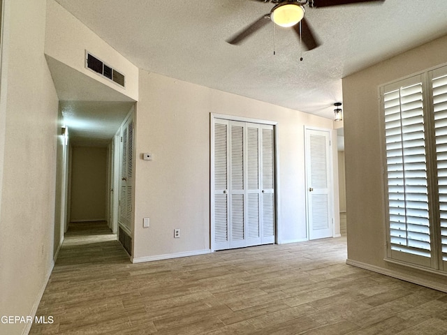 unfurnished bedroom with hardwood / wood-style floors, ceiling fan, a textured ceiling, and multiple closets