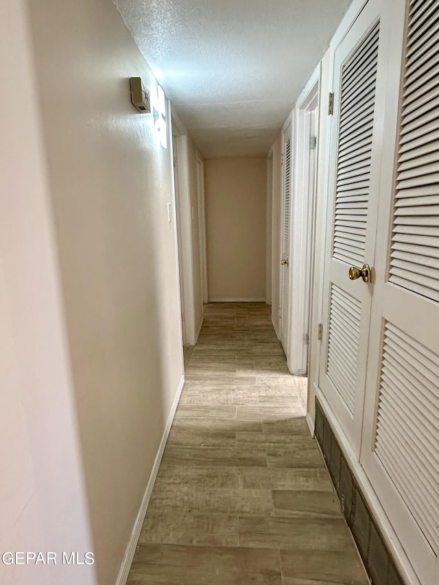 hallway featuring light wood-type flooring and a textured ceiling