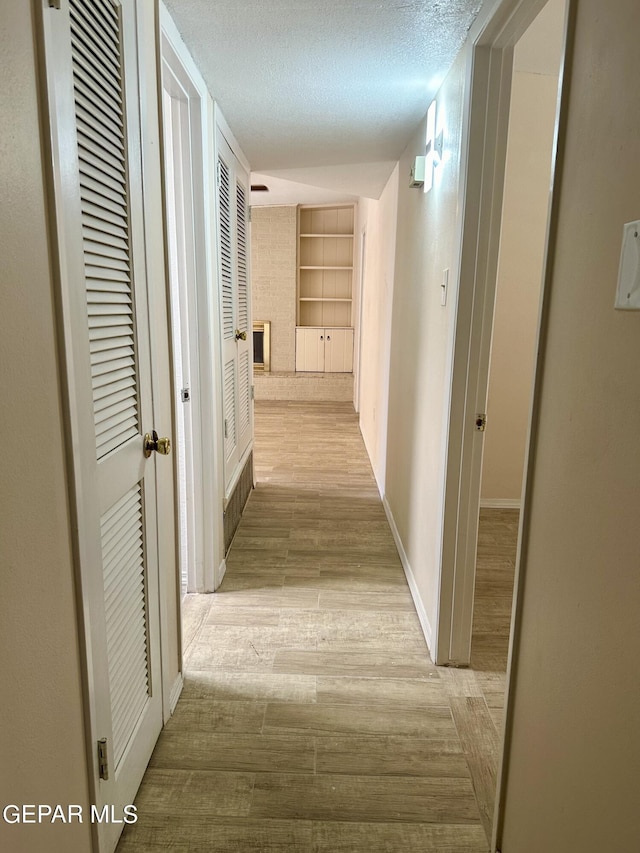 corridor featuring built in shelves, a textured ceiling, and light hardwood / wood-style flooring