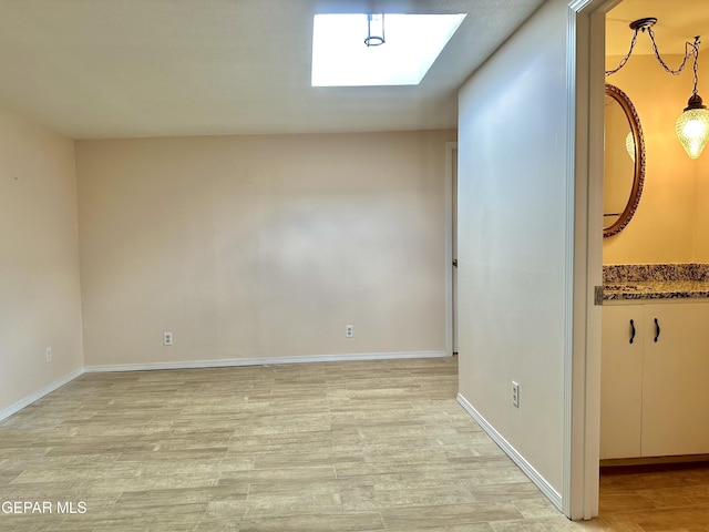 unfurnished room with a skylight and light hardwood / wood-style flooring