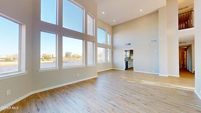 unfurnished living room featuring a towering ceiling and light hardwood / wood-style flooring