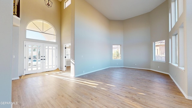 foyer entrance with a high ceiling, an inviting chandelier, light hardwood / wood-style flooring, and french doors