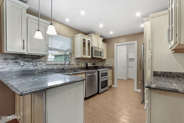 kitchen with sink, hanging light fixtures, dark stone countertops, appliances with stainless steel finishes, and light wood-type flooring