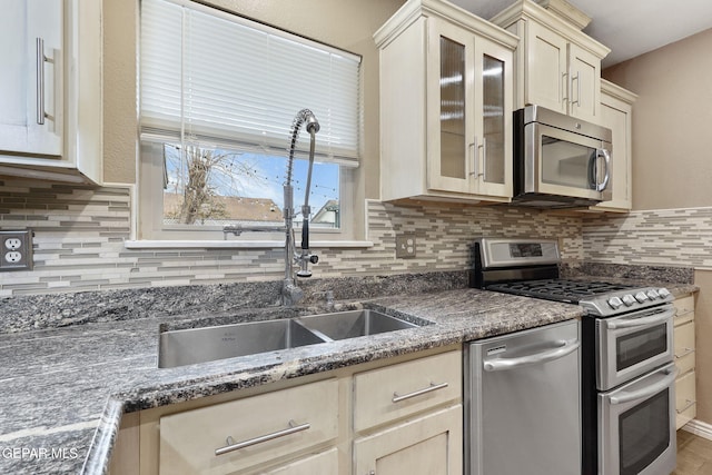 kitchen featuring dark stone counters, cream cabinets, sink, tasteful backsplash, and stainless steel appliances