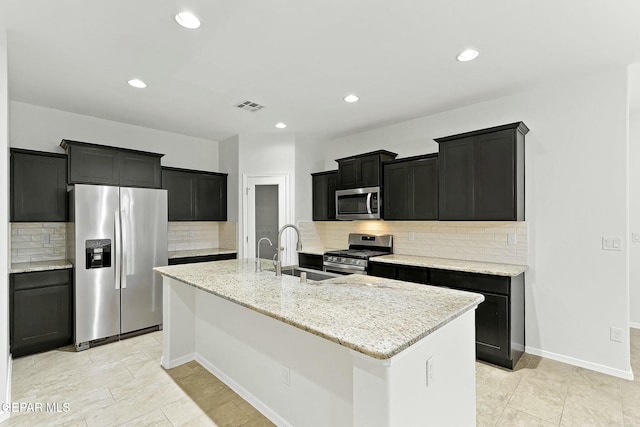 kitchen featuring light stone countertops, tasteful backsplash, stainless steel appliances, sink, and a center island with sink