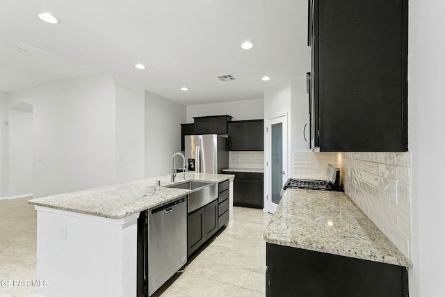 kitchen featuring backsplash, light stone countertops, a kitchen island with sink, and appliances with stainless steel finishes