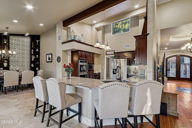 kitchen with kitchen peninsula, a breakfast bar area, stainless steel appliances, decorative light fixtures, and french doors