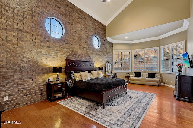 bedroom with brick wall, light hardwood / wood-style floors, ornamental molding, and high vaulted ceiling