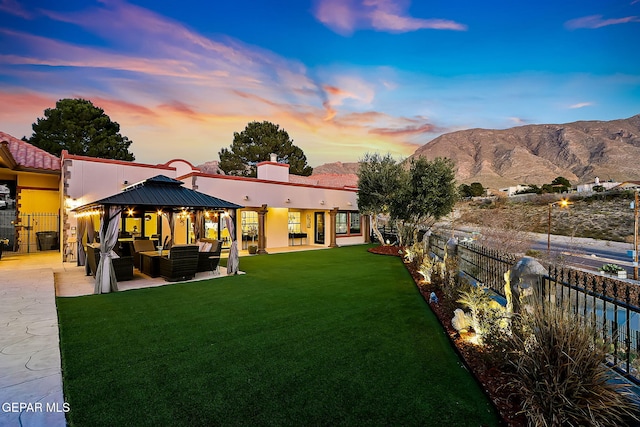 back house at dusk with an outdoor living space, a patio area, a lawn, a mountain view, and a gazebo