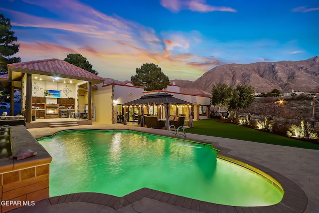 pool at dusk featuring a mountain view, a gazebo, a yard, area for grilling, and a patio