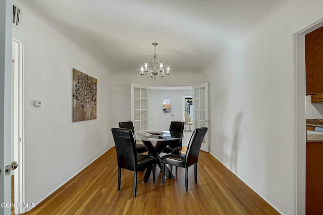 dining space featuring french doors, hardwood / wood-style flooring, and a notable chandelier