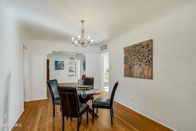 dining area featuring built in shelves, hardwood / wood-style floors, and an inviting chandelier