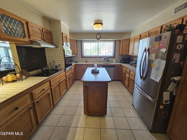 kitchen with a center island, tasteful backsplash, a textured ceiling, light tile patterned floors, and appliances with stainless steel finishes