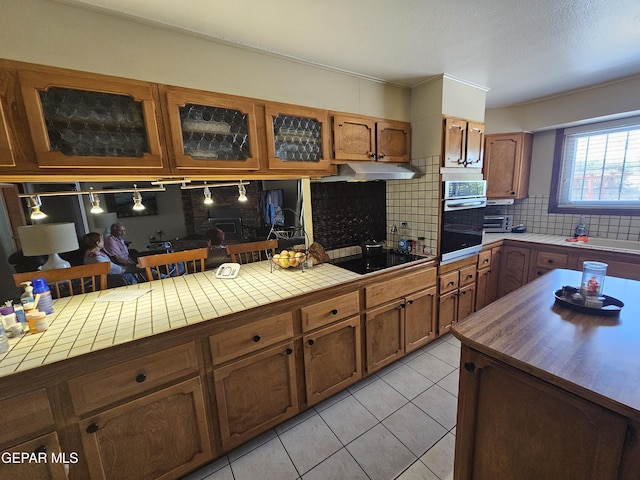 kitchen featuring tile countertops, stainless steel oven, backsplash, black electric cooktop, and light tile patterned floors