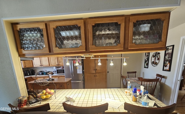 kitchen featuring stainless steel fridge, backsplash, and tile countertops