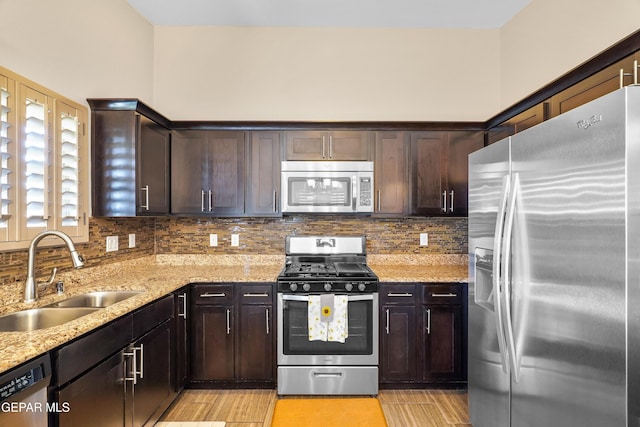 kitchen featuring appliances with stainless steel finishes, dark brown cabinets, light stone counters, and sink