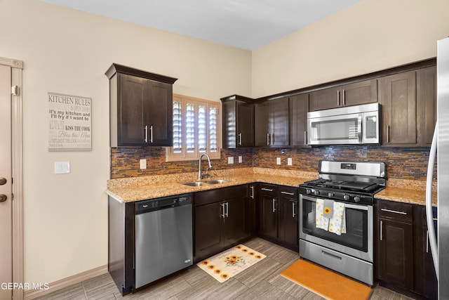 kitchen featuring appliances with stainless steel finishes, backsplash, light stone counters, dark brown cabinetry, and sink