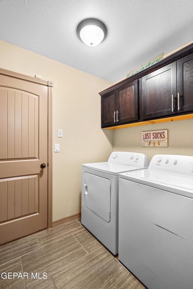 washroom featuring cabinets, a textured ceiling, and washer and clothes dryer