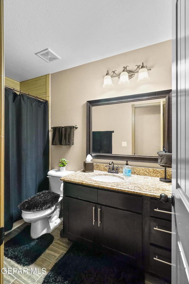 bathroom with toilet, a textured ceiling, walk in shower, and vanity