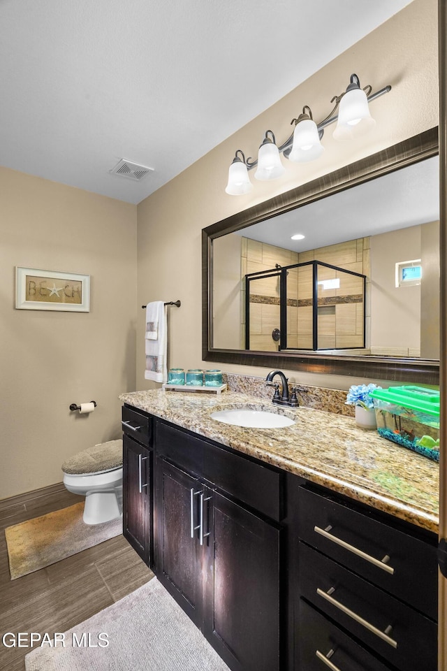 bathroom featuring a shower with shower door, toilet, and vanity