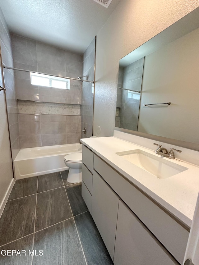 full bathroom featuring tiled shower / bath combo, tile patterned flooring, a textured ceiling, toilet, and vanity