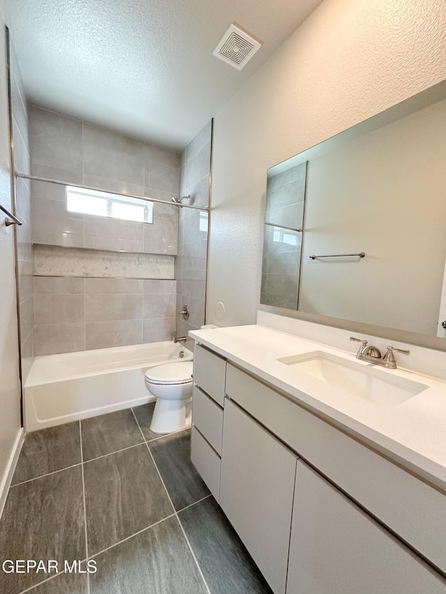 full bathroom with vanity, tile patterned floors, tiled shower / bath combo, toilet, and a textured ceiling