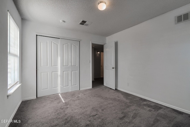 unfurnished bedroom with a closet, dark carpet, and a textured ceiling