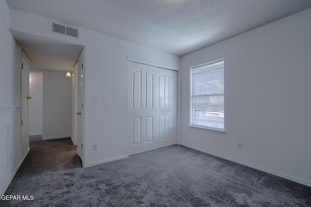 unfurnished bedroom featuring a closet, dark carpet, and a textured ceiling