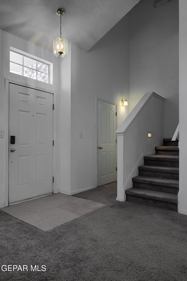 carpeted entryway featuring a textured ceiling, a towering ceiling, and a notable chandelier