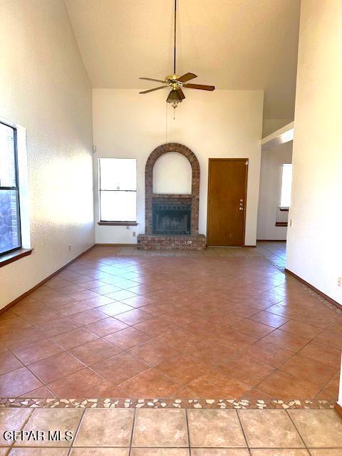 unfurnished living room with tile patterned flooring, ceiling fan, a healthy amount of sunlight, and a brick fireplace