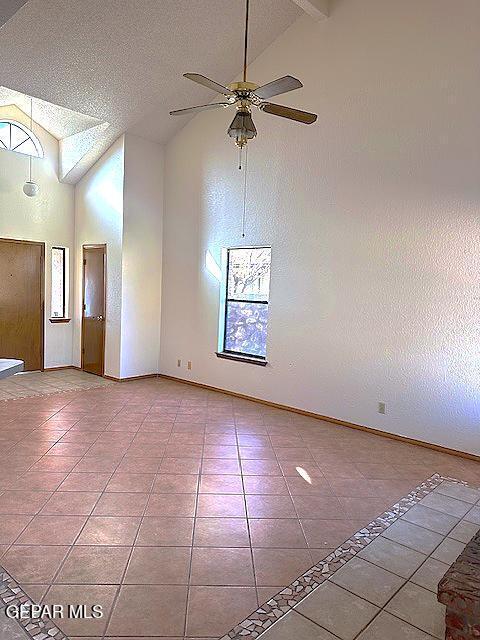 tiled empty room with beam ceiling, a textured ceiling, high vaulted ceiling, and ceiling fan