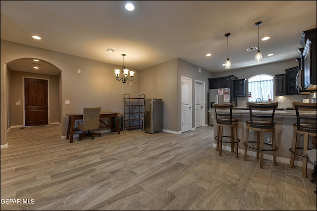 kitchen with hanging light fixtures, backsplash, a chandelier, light hardwood / wood-style floors, and a breakfast bar