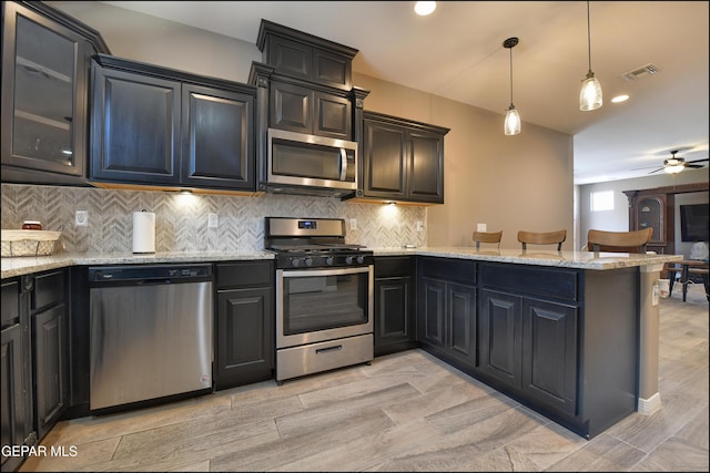 kitchen featuring pendant lighting, ceiling fan, light stone countertops, appliances with stainless steel finishes, and kitchen peninsula