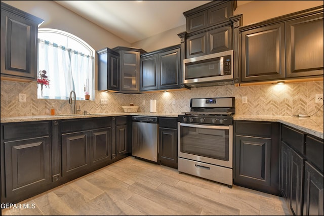 kitchen with appliances with stainless steel finishes, backsplash, light stone counters, and sink