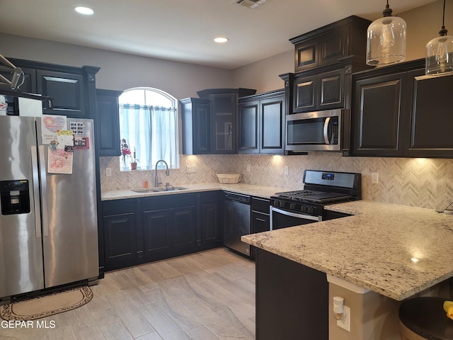 kitchen featuring sink, hanging light fixtures, light stone counters, light hardwood / wood-style flooring, and appliances with stainless steel finishes