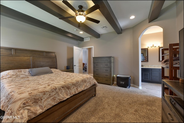 carpeted bedroom with beamed ceiling, ceiling fan, and ensuite bath