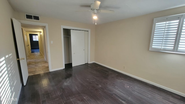 unfurnished bedroom with multiple windows, dark wood-type flooring, a closet, and ceiling fan