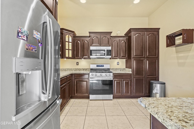 kitchen featuring stainless steel appliances, light stone countertops, dark brown cabinetry, and light tile patterned flooring