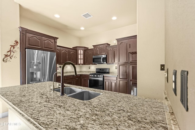 kitchen featuring light stone counters, recessed lighting, a sink, dark brown cabinetry, and appliances with stainless steel finishes