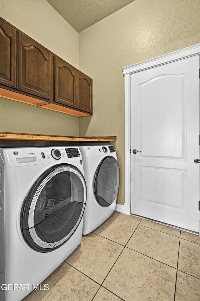 clothes washing area with light tile patterned floors, cabinet space, a textured ceiling, and washing machine and clothes dryer