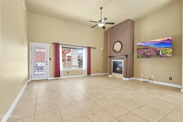 unfurnished living room with light tile patterned floors, baseboards, a high ceiling, a fireplace, and ceiling fan