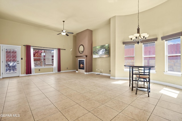 unfurnished living room featuring ceiling fan with notable chandelier, a glass covered fireplace, light tile patterned floors, baseboards, and a towering ceiling