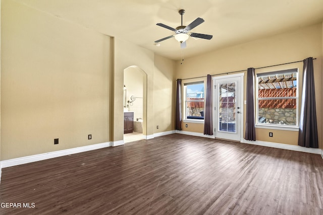 spare room with arched walkways, baseboards, a ceiling fan, and dark wood-style flooring