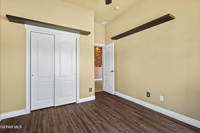 unfurnished bedroom featuring a closet, lofted ceiling, dark wood-type flooring, and baseboards