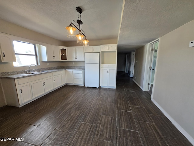 kitchen with white refrigerator, white cabinetry, hanging light fixtures, and sink