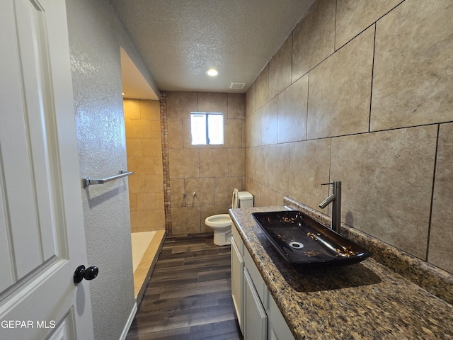 bathroom with vanity, hardwood / wood-style flooring, toilet, a textured ceiling, and tile walls